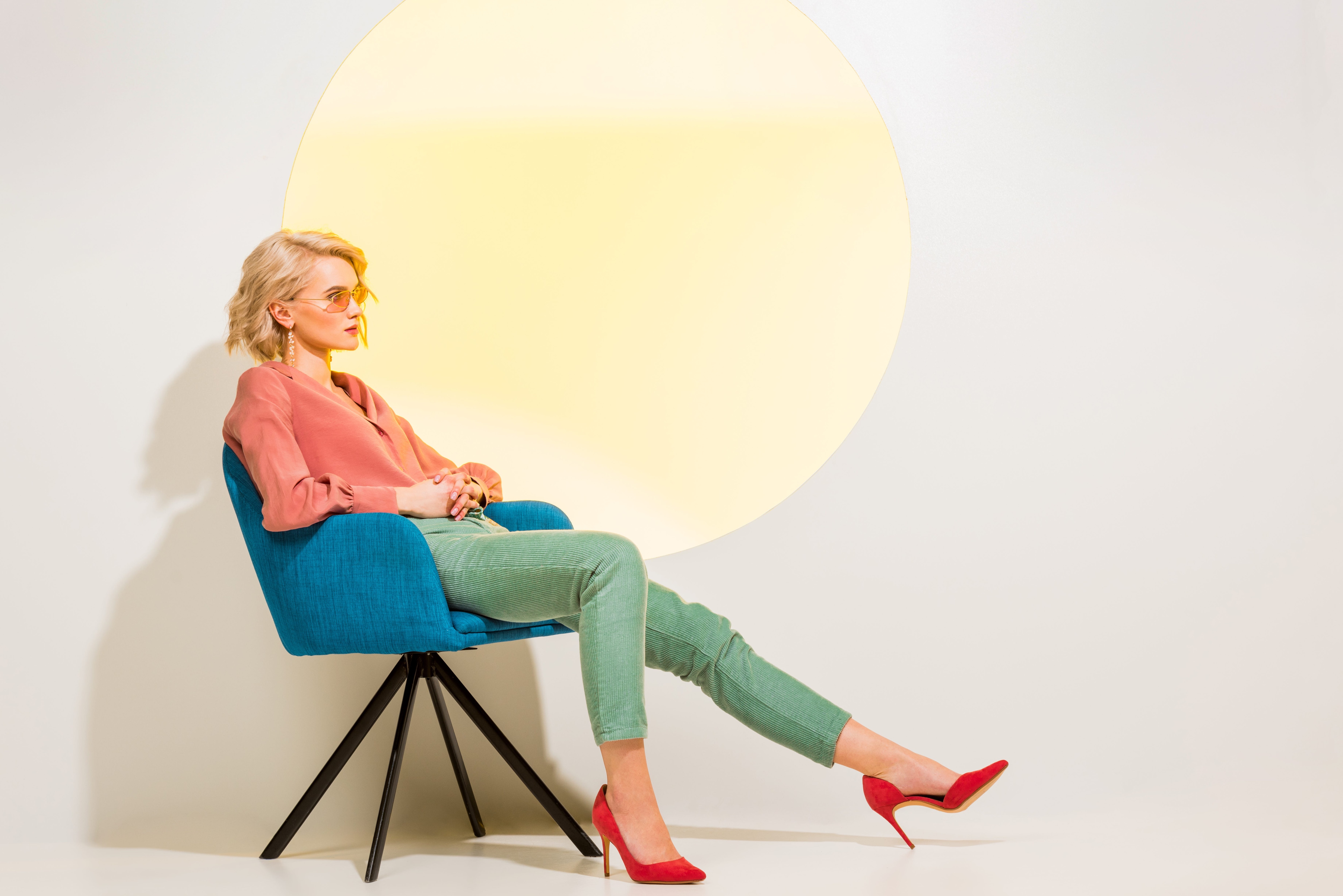 Blonde woman sitting on a chair while wearing accessories, including sunglasses, earrings, and sleek pumps.jpeg